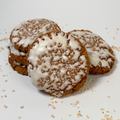 Five round oatmeal cookies with white icing drizzle, arranged on a white surface with scattered oat flakes.